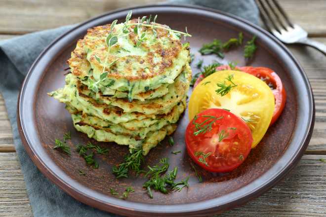 frittelle di zucchine su un piatto, con pomodori freschi